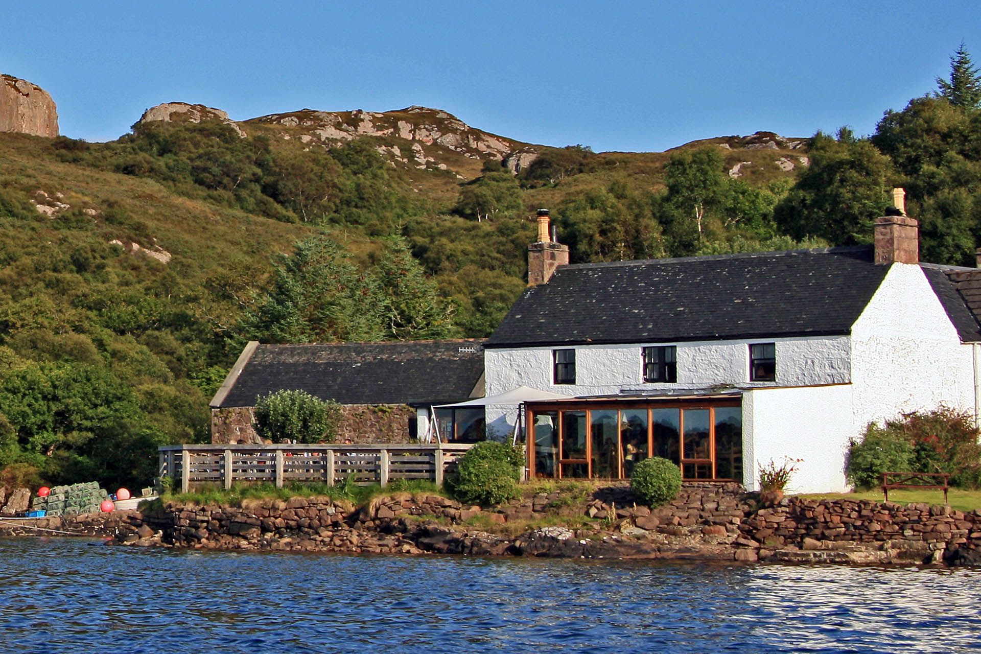 A picture taken from the sea of the outside of the Badachro Inn in Gairloch. The Inn is a large white washed cottage in style