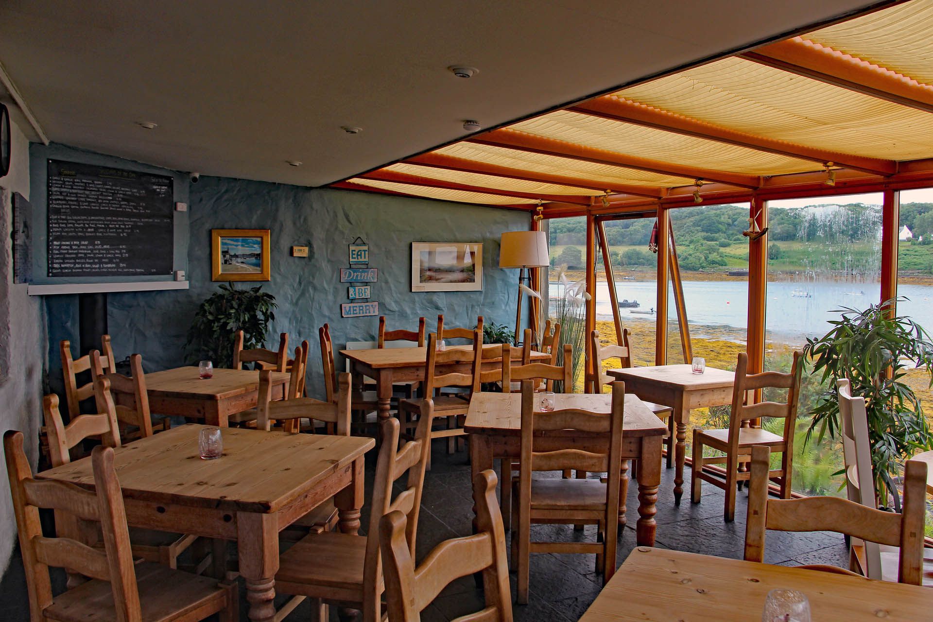 A picture of the seating area within the Badachro Inn in Gairloch. The picture includes a selection dining tables with a view of the estuary and a specials board.