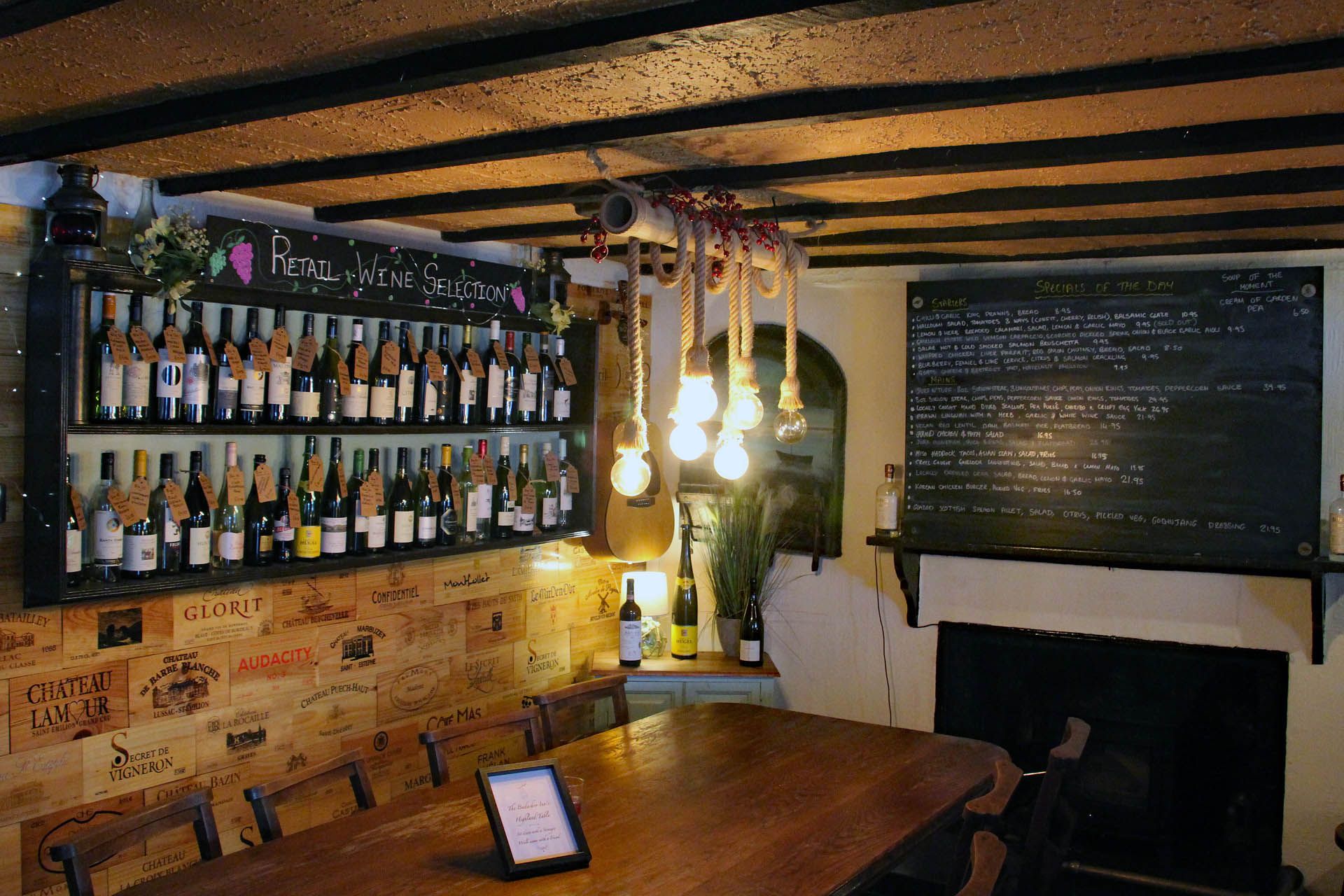 A picture of the seating area within the Badachro Inn in Gairloch. The picture includes a selection of wines, a large dining table and a specials board.