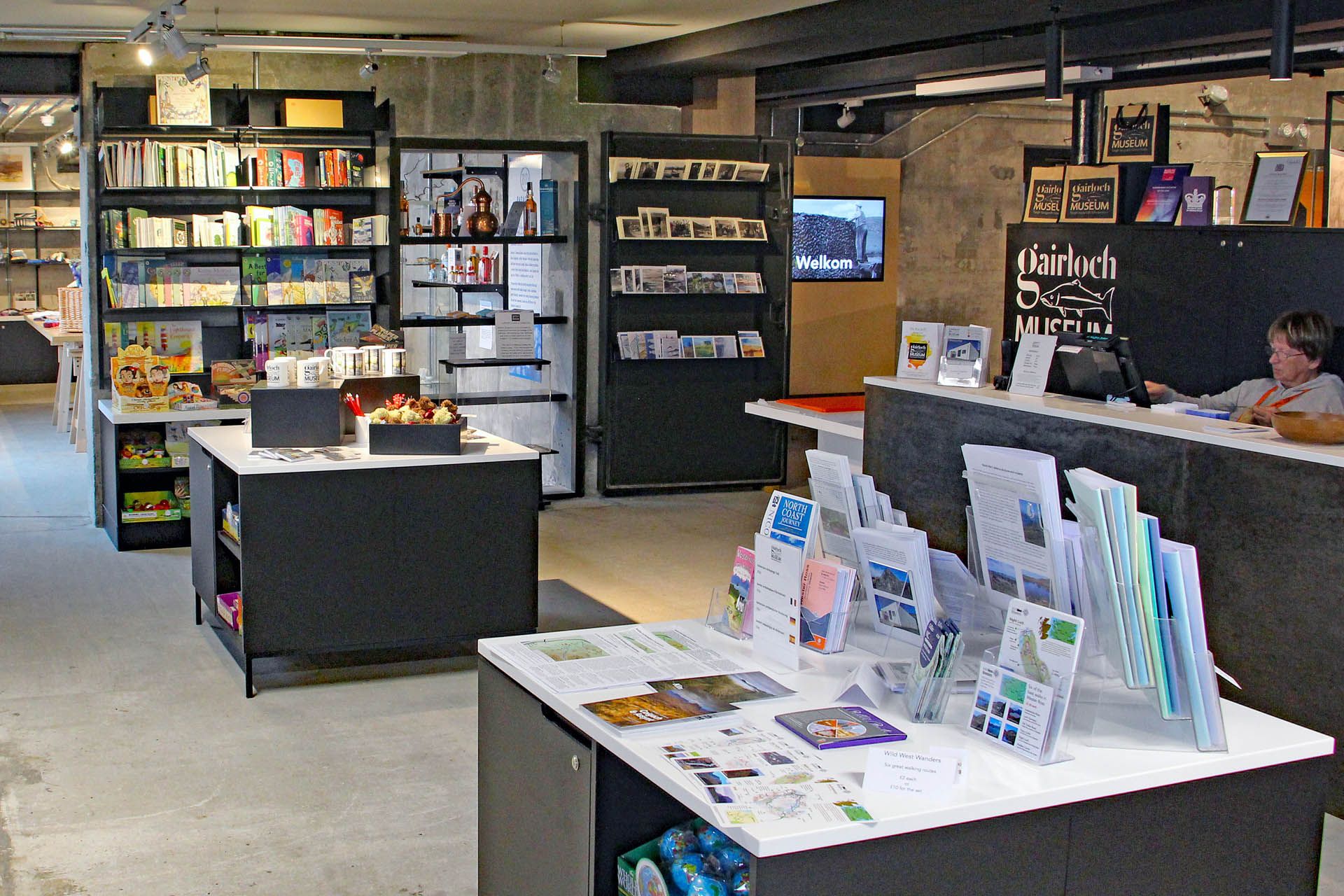 A picture of the gift store and reception at the Gairloch Museum. The picture features books, leaflets and a reception counter with an employee working on a computer behind a desk