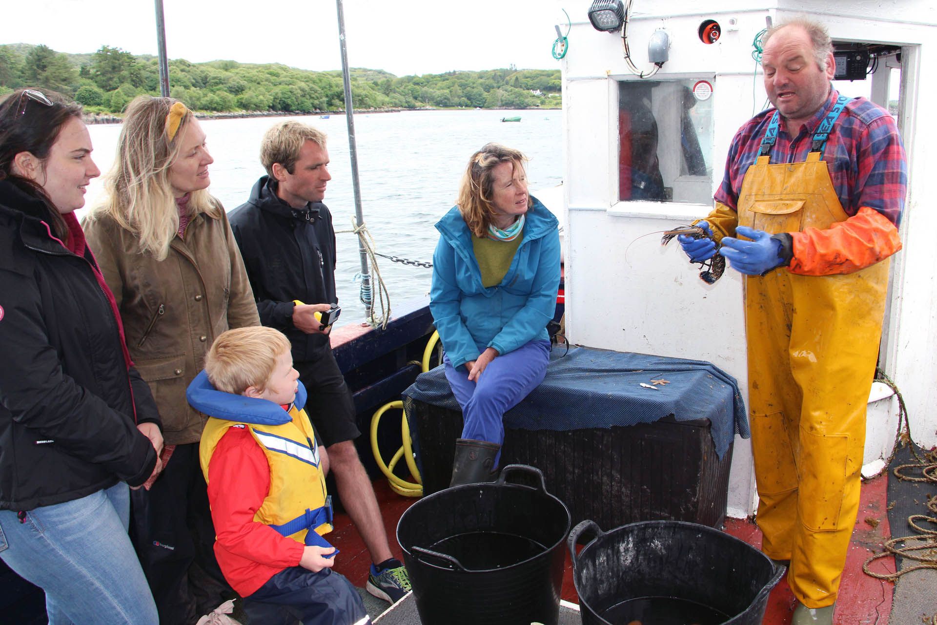 Picture of a fisherman on a boat holding a shell fish and providing a talk to people on a tour