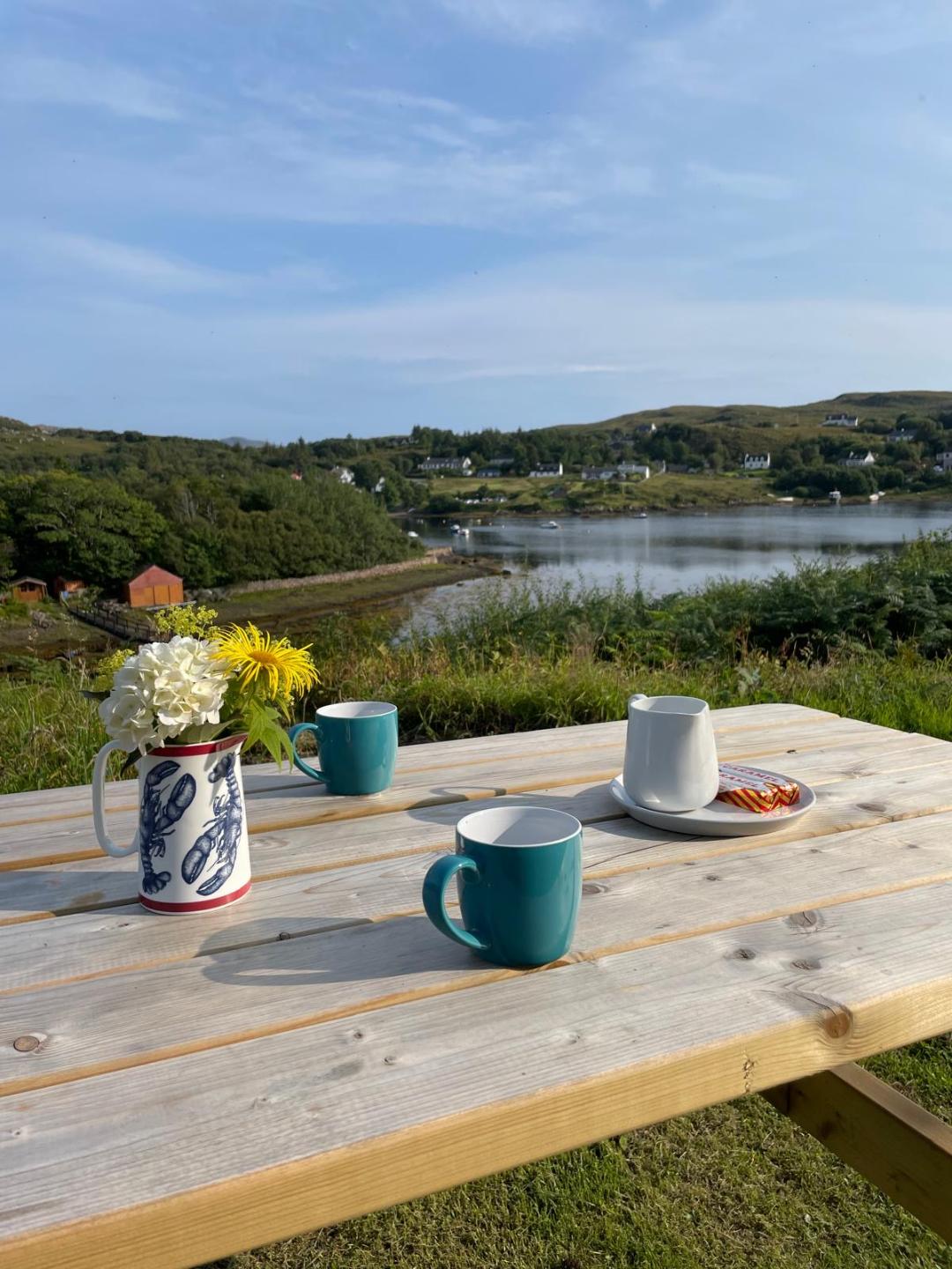 A view of Badachro from Aird Cottage. The image features a table with tea mugs in the foreground.
